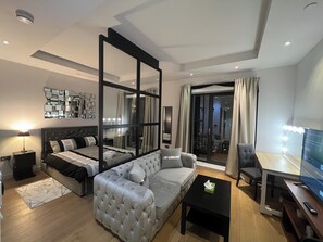 Una sala moderna con una cama grande, un sofá gris, una mesa de centro negra y un televisor.