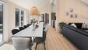 En modern inredning med ett långt matbord, svarta stolar, en grå soffa och träväggar.