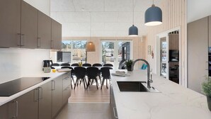 Ett modernt kök med en köksö i mitten, en matplats med stolar och ett stort fönster.