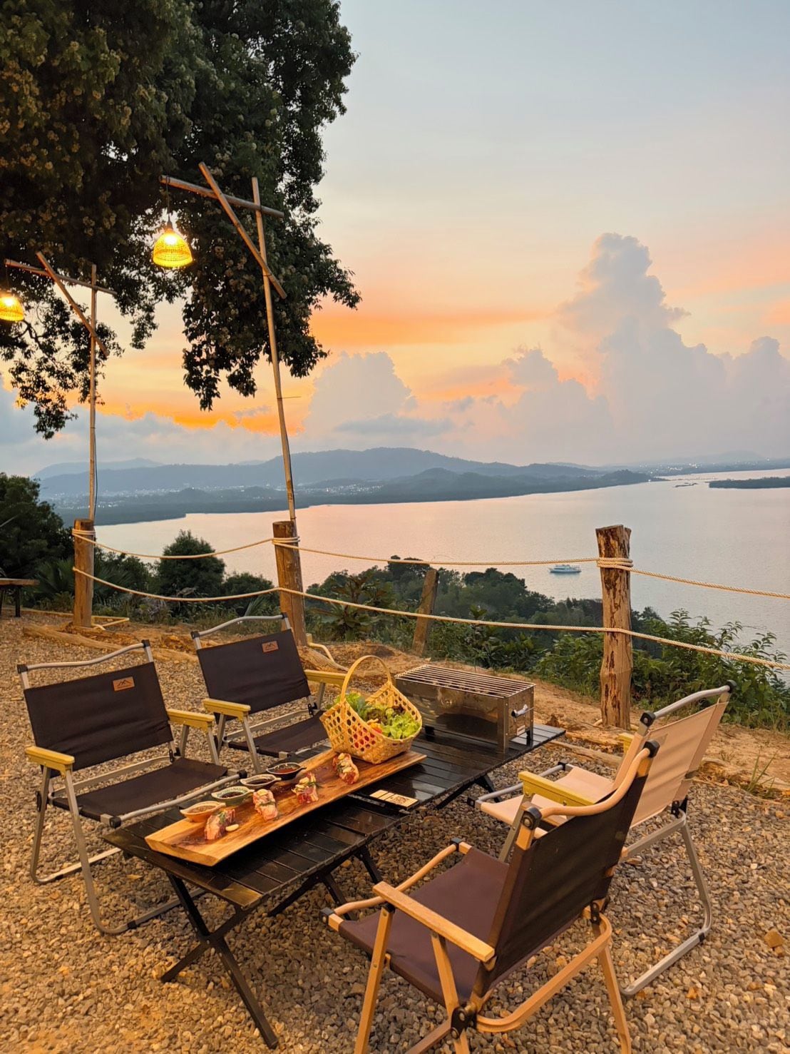 An outdoor seating area with chairs and a table, overlooking a body of water and distant mountains.