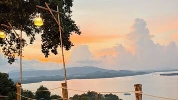 An outdoor seating area with chairs and a table, overlooking a body of water and distant mountains.