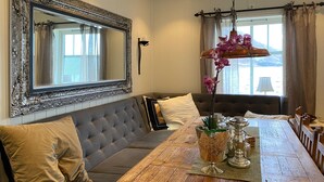 A dining area with a wooden table, a sofa with cushions, a large mirror, and a hanging orchid light fixture.