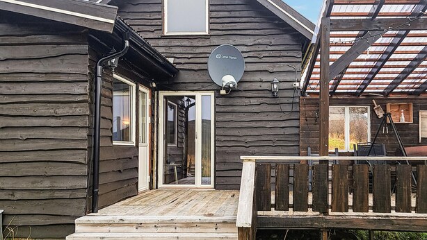 Eine rustikale Holzhütte mit einer Holzdielen-Terrasse, einer Satellitenschüssel und einem kleinen Fenster.