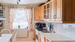 Eine Küche mit Holzausstattung, einer weißen Arbeitsplatte, einem Spülbecken und einem Fenster mit blumigen Vorhängen.