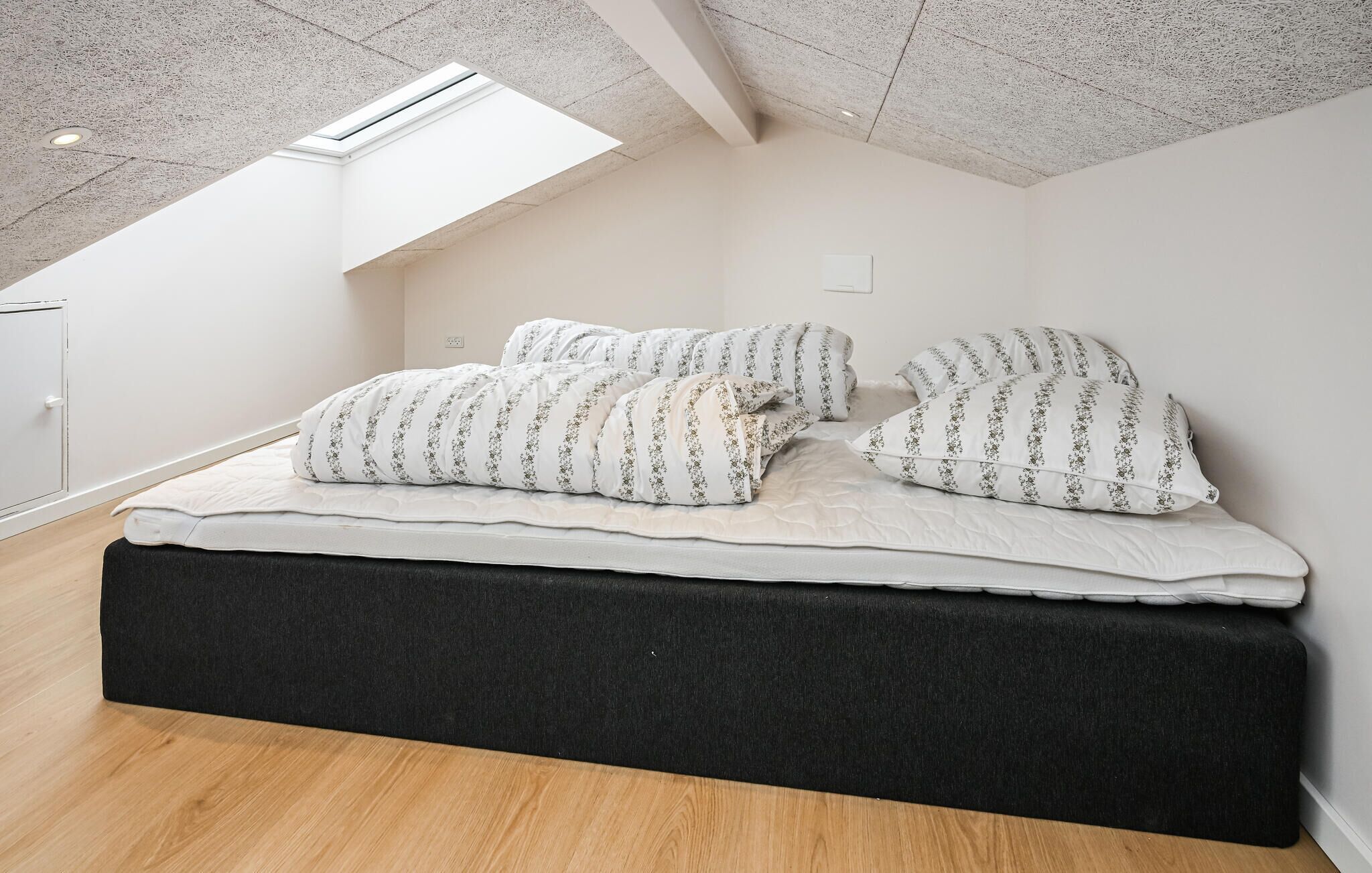A bedroom with a sloped ceiling, a skylight, a bed with white bedding, and a dark headboard.