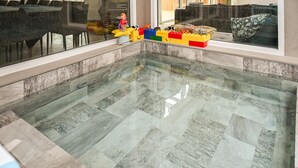 A clear glass-bottomed pool with a tiled floor, surrounded by a seating area with a sofa and a window.