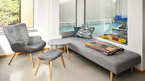 A modern room with a grey sofa, a matching armchair, a small round table, and a bench with a colorful quilt.