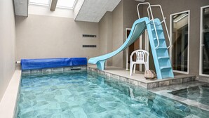 An indoor pool with a blue slide, a white chair, and a stone on the edge.