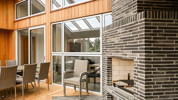 A patio with wicker chairs and a table, a brick fireplace, and large windows.