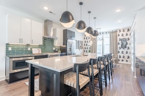 A modern kitchen with a central island, bar stools, pendant lights, and a patterned wallpaper design. - Lucile 83 85 Double (Nashville)
