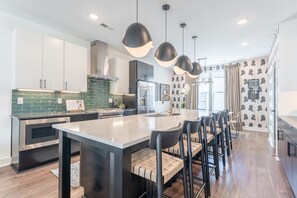 A modern kitchen with a central island, bar stools, pendant lighting, and a patterned wallpaper design. - Lucile 83 85 Double (Nashville)