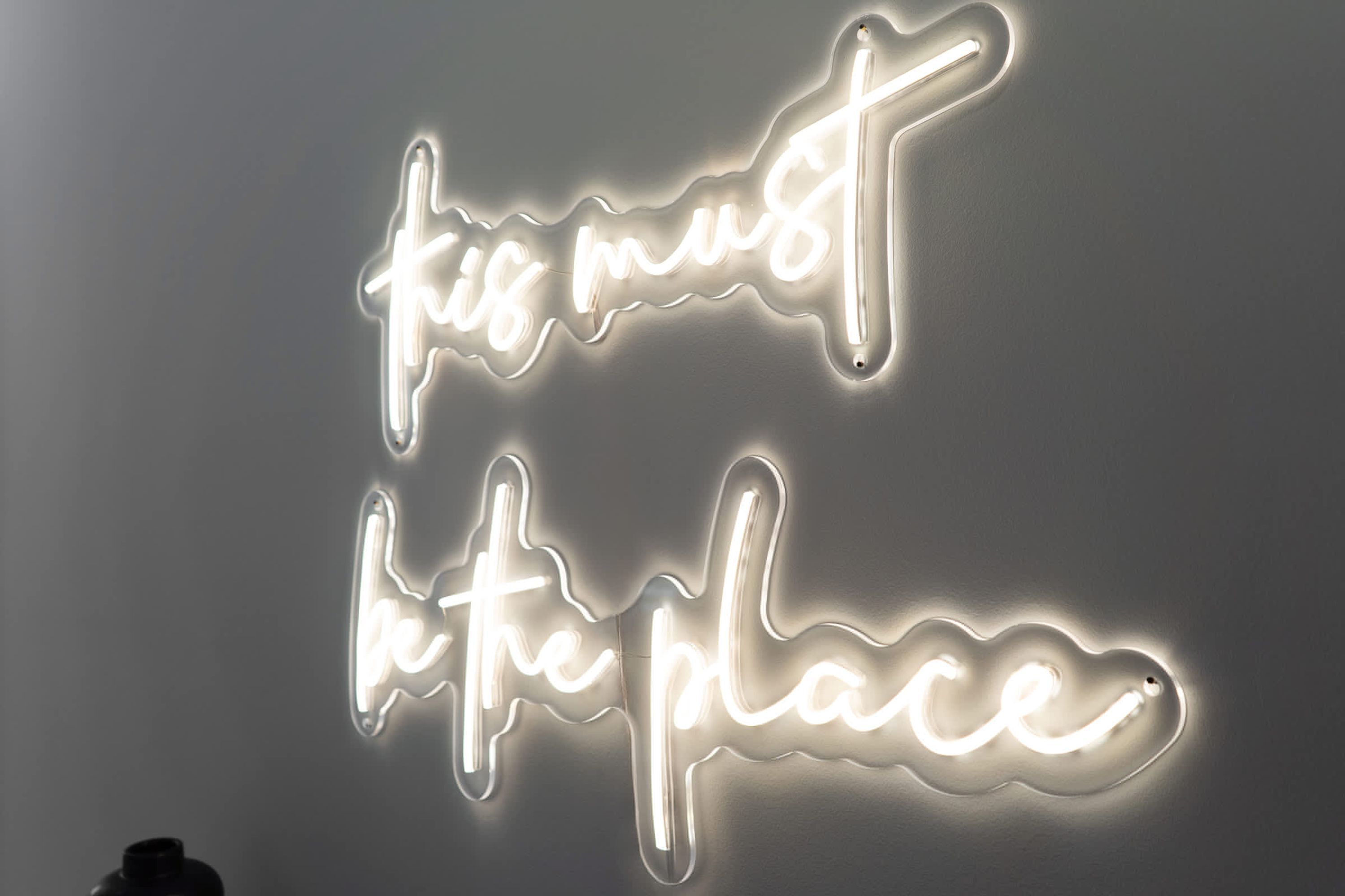 A neon sign with the text "this must be place" on a plain wall.