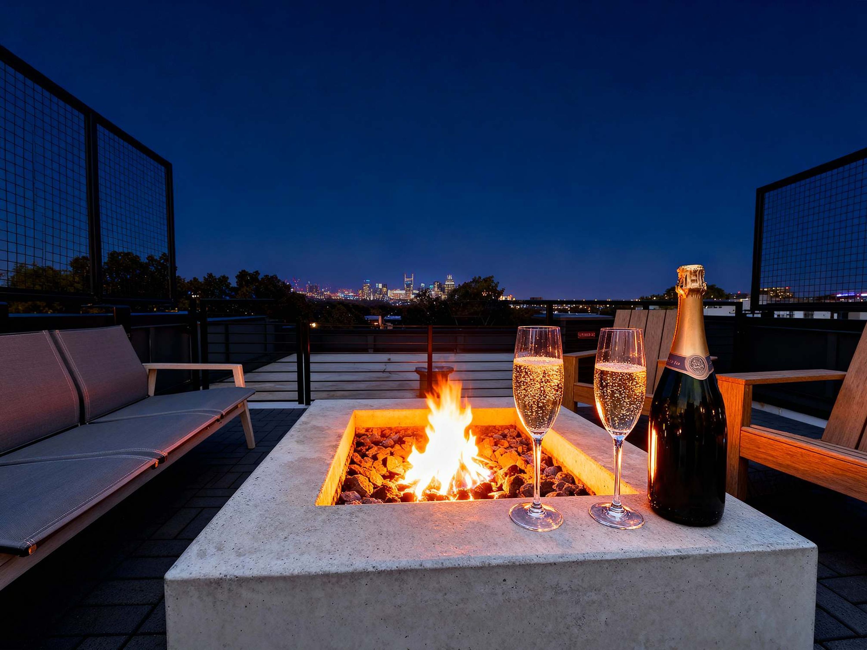 A rooftop terrace with a fire pit, two glasses of champagne, and a bottle of champagne.