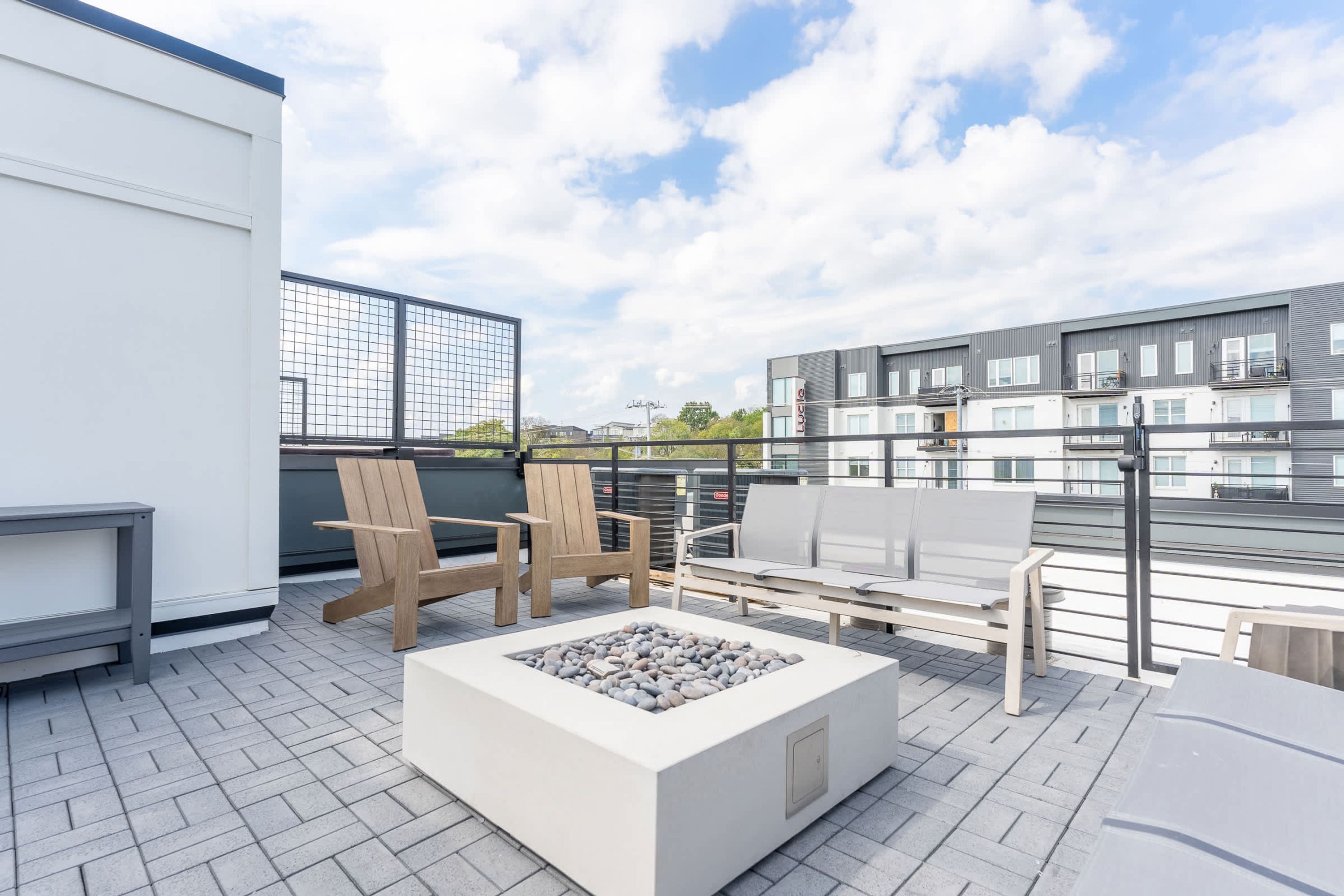 A rooftop terrace with outdoor seating, a fire pit, and a view of modern buildings.