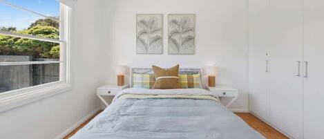 A bedroom with a bed, bedside tables, a wardrobe, and two wall-mounted artworks.