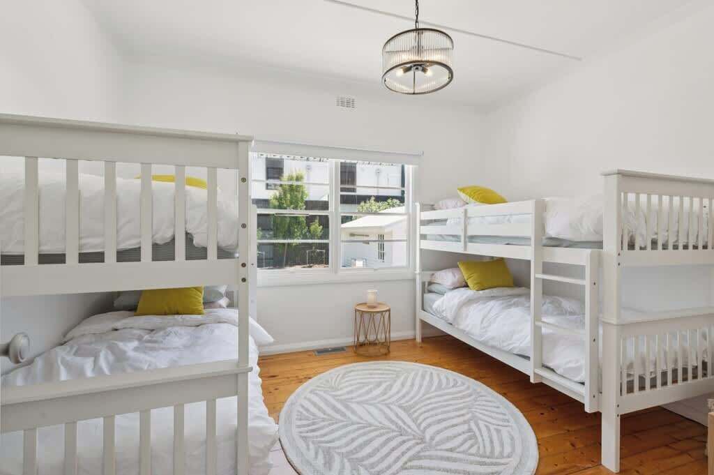 A room with bunk beds, a round rug, and a window with a view of buildings outside.