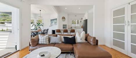 A modern living room with a sectional sofa, a coffee table, and a dining area in the background.