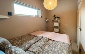Un dormitorio con cama, ventana, lámpara colgante y estante con plantas.