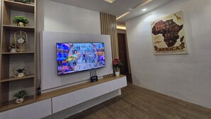 Ett modernt vardagsrum med en platt-TV som är monterad på en vit vägg, trähyllor med dekorativa föremål, ett träbord och ett väggmonterat konstverk som föreställer Afrika.