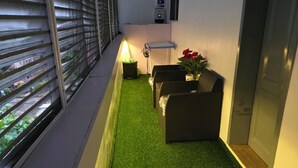 En smal korridor med konstgjord, grön matta, ett litet bord med en lampa och möbler av rotting.