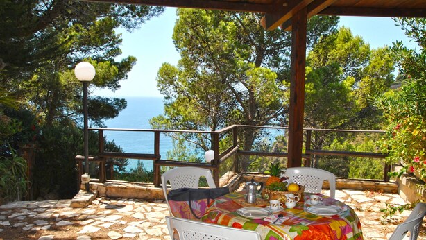 An outdoor dining area with a table set for two, overlooking a scenic view of the sea and trees. - Marilena cottage between sea and nature (Sperlonga)