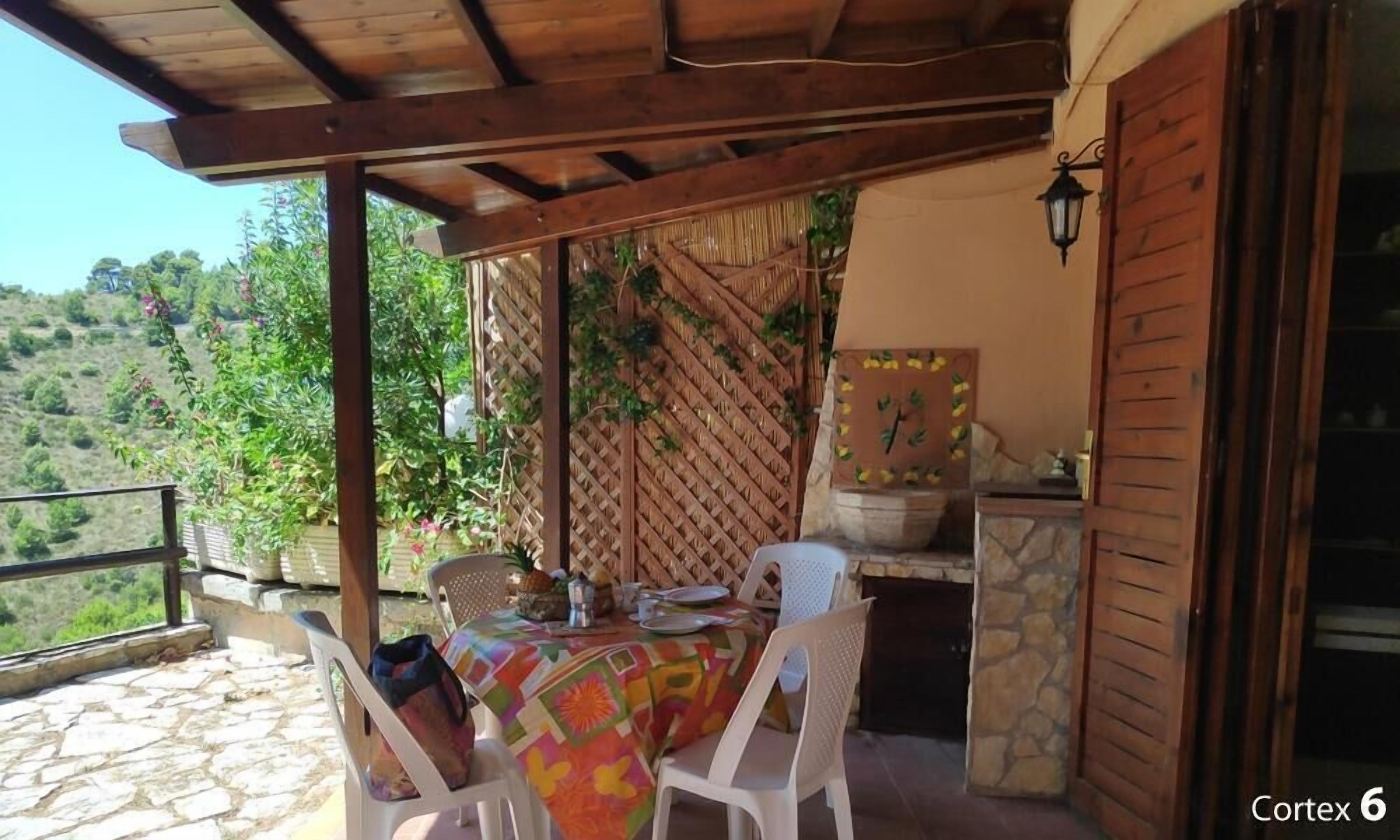 An outdoor patio with a table set for two, surrounded by stone walls and a wooden pergola.