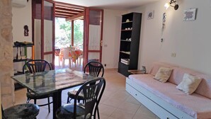 A dining area with a glass table and chairs, a sofa, a bookshelf, and a door leading outside. - Marilena cottage between sea and nature (Sperlonga)