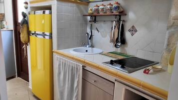 Een keuken met een gele koelkast, een spoelbak en een fornuis. Er staan decoratieve items op de muur en er is een raam boven de spoelbak.