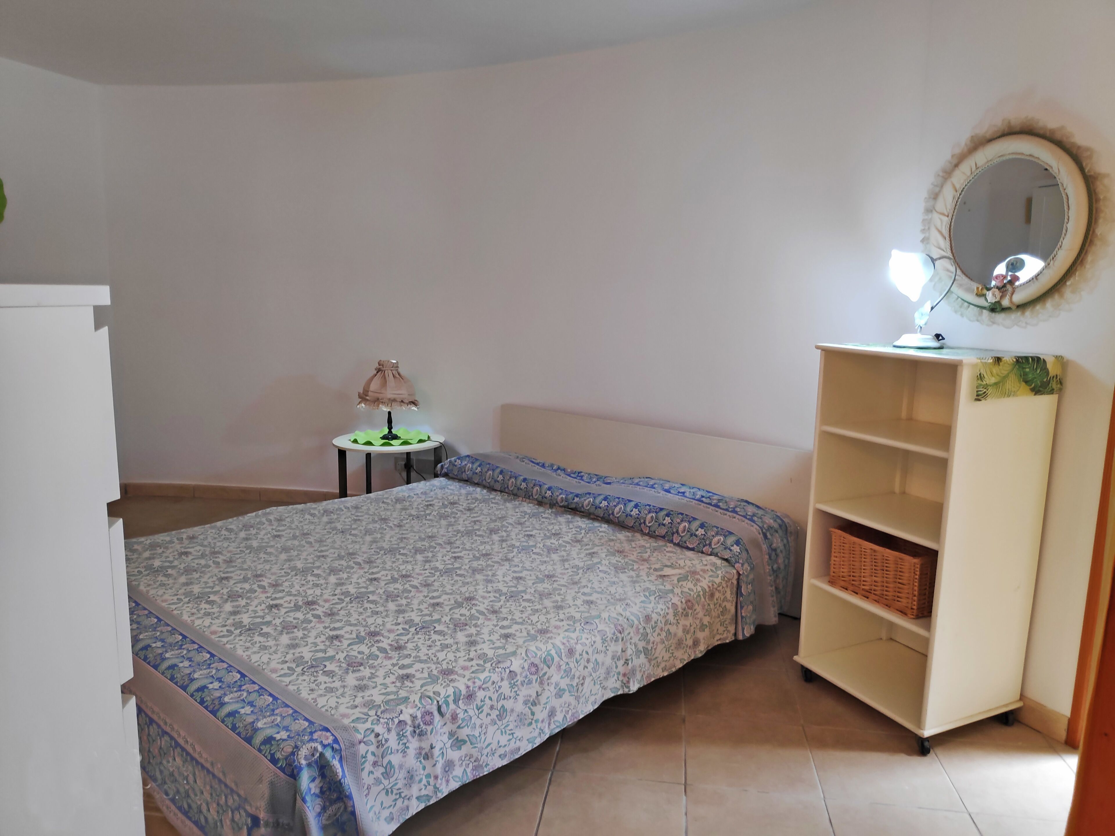 A bedroom with a bed, a bedside table with a lamp, a mirror, and a wardrobe.