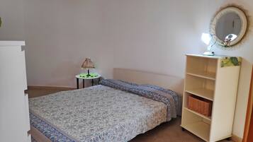 A bedroom with a bed, a bedside table with a lamp, a mirror, and a wardrobe.