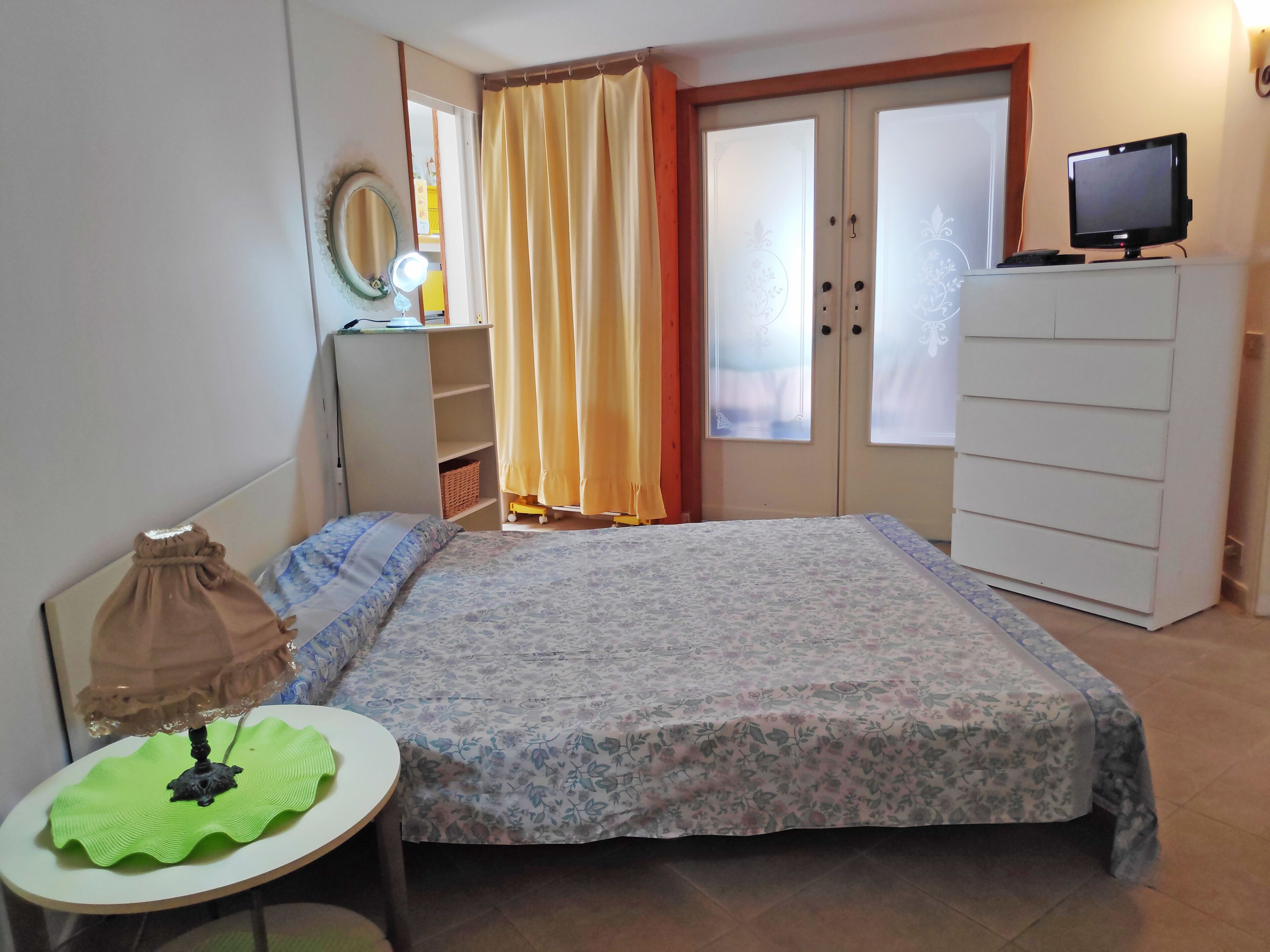 Ein Schlafzimmer mit Bett, Schreibtisch, Kommode, Spiegel und Fernseher.