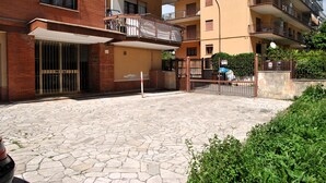 Un edificio residencial de varios pisos con balcones, una entrada con portón y un patio empedrado.