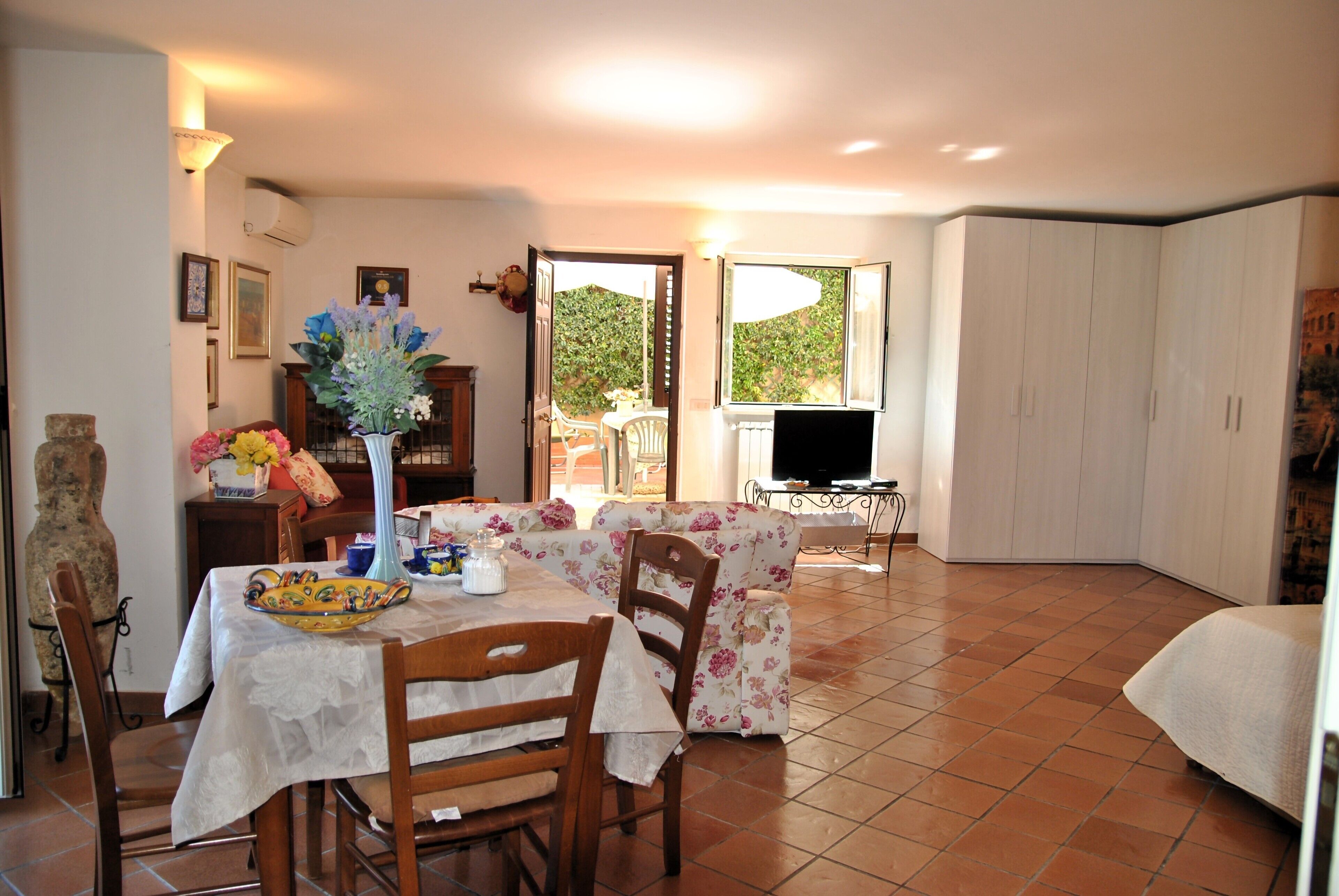 A dining area with a table set for two, a floral sofa, and a television in the background.