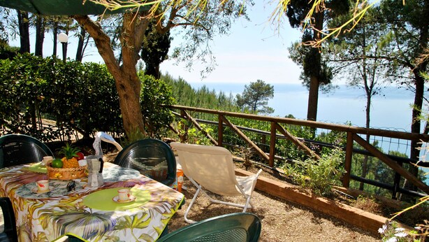 An outdoor dining area with a table set for two, surrounded by chairs, overlooking a scenic view of the sea.