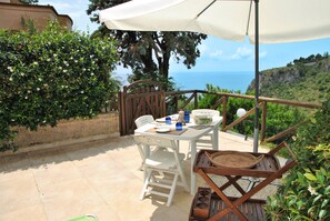 An outdoor patio with a table and chairs, a white umbrella, and a view of the sea. - Casa Ancoretta Green Hills and Sea (Sperlonga)