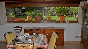 Un comedor con una mesa preparada para cuatro personas, un aparador de madera y una ventana con plantas en macetas.
