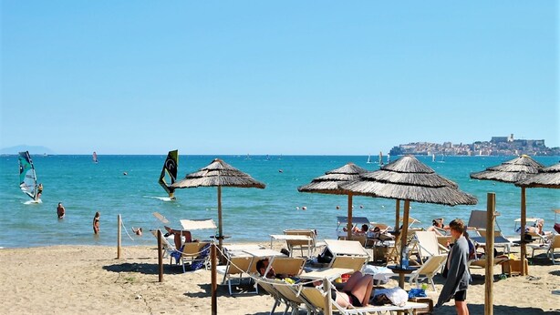 Una playa con tumbonas, sombrillas y vistas al mar y una ciudad lejana.