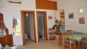 A dining area with wooden chairs and a table covered by a floral tablecloth. There is a wooden cabinet and a mirror on the left. - Casa Simon Nature and Sea (Sperlonga)