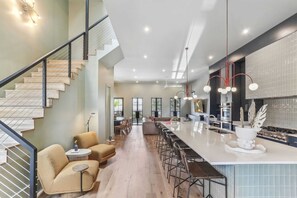 A modern kitchen with a large island, bar stools, and a staircase with a railing. - LGD Luxury Combo | Heated Pool & Hot Tub (New Orleans)