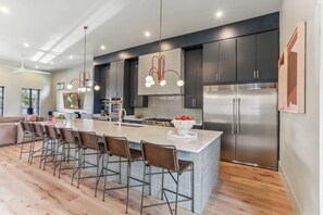 A modern kitchen with a large island, dark cabinetry, stainless steel appliances, and a pendant light fixture. - LGD Luxury Combo | Heated Pool & Hot Tub (New Orleans)