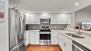 A modern kitchen with stainless steel appliances, white cabinetry, and a granite countertop. - Bayside Endless Summer | Walk to Siesta Key Beach, Community Pool, & Tennis Court (Siesta Key)