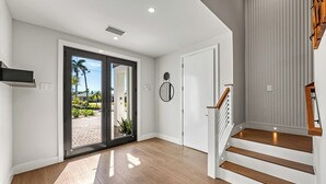 Ein modernes Interieur mit einer Holztreppe, einer Tür zu einem Außenbereich und einem hellen Boden.