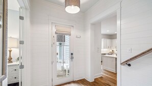 A hallway with white paneled walls, a wooden floor, a door leading to a balcony, and a kitchen area visible through an open door. - Watersound~ Golf Cart | Bikes | Gated Community | Private Beach Access (Santa Rosa Beach)
