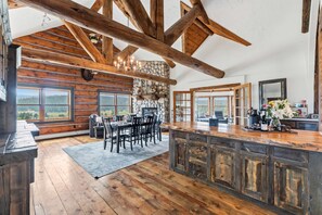 Ein rustikales Interieur mit Holzbalken, einem Kamin aus Stein, einem Essbereich und großen Fenstern mit Blick.