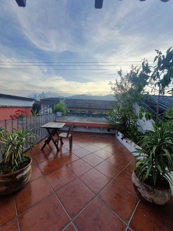 Terraza en la azotea con una mesa, sillas, plantas en macetas y vistas a montañas distantes.