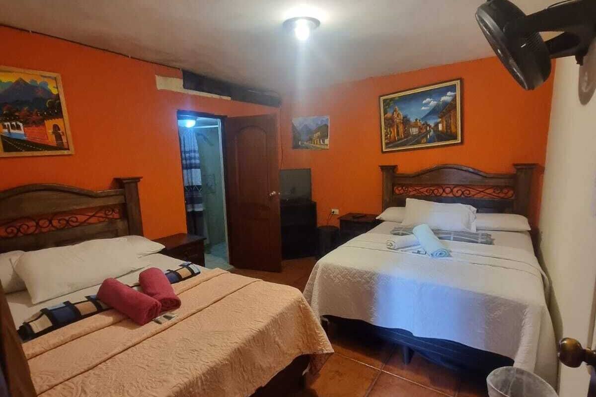 A room with two beds, a ceiling fan, and a door leading to another room.