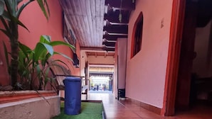 A corridor with artificial grass, a blue trash bin, and a wooden ceiling. - Hotel Ciudad de los sueños (Antigua Guatemala)