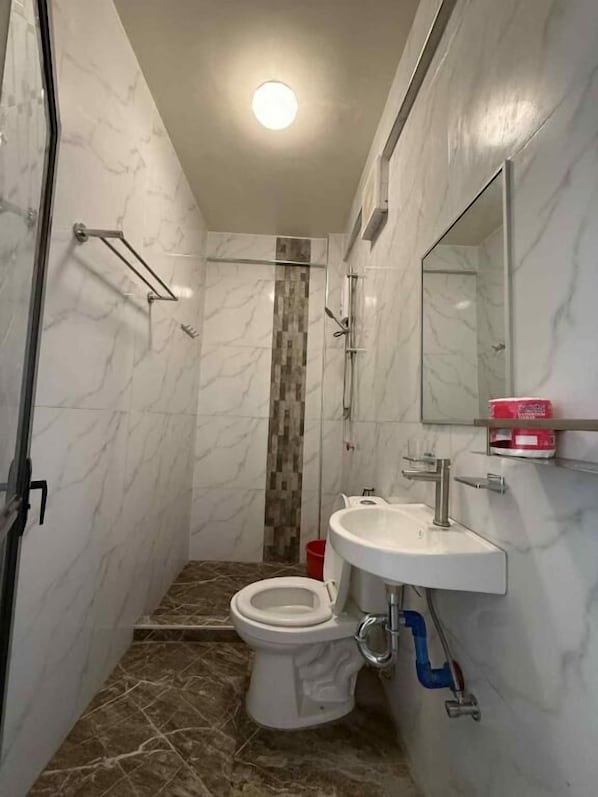 A bathroom with a toilet, sink, shower, and a mirror.