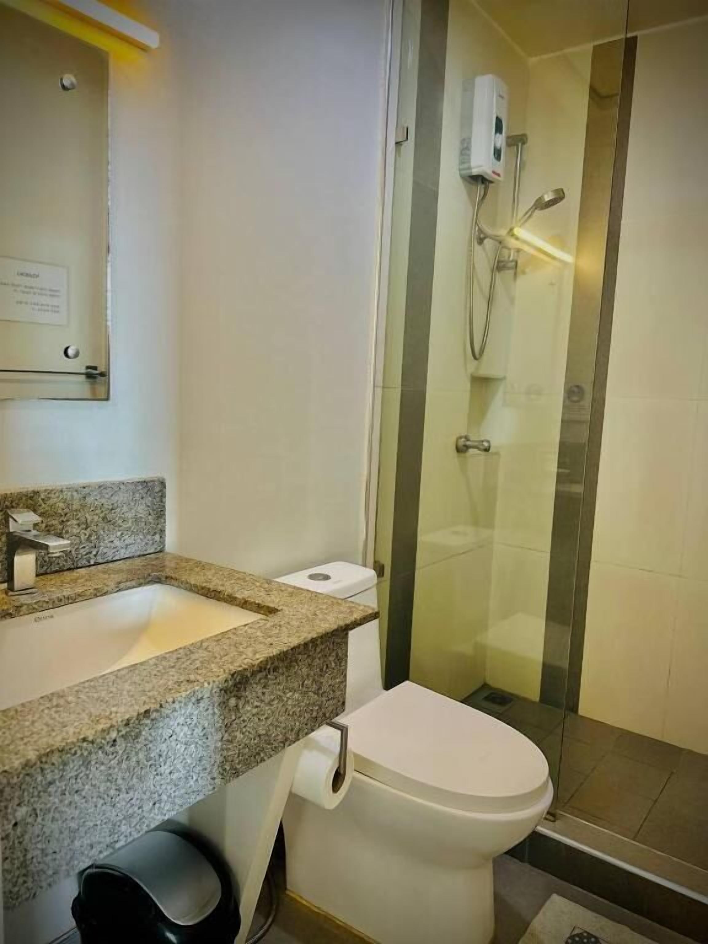 A bathroom with a granite countertop sink, a toilet, and a glass-enclosed shower area.