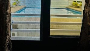 A window view of a pool area with a clear sky and a distant island. - Playa Blanca Beach Resort & Dive Centre (Puerto Galera)